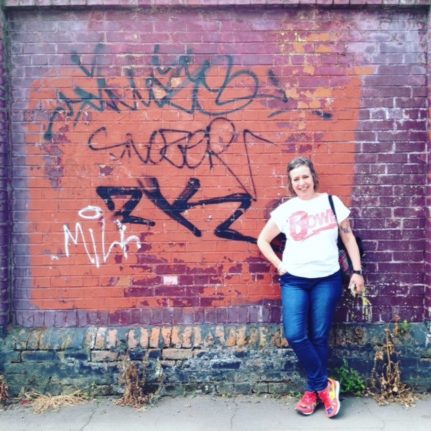 Image is a photos of Mairi standing next to a graffiti wall