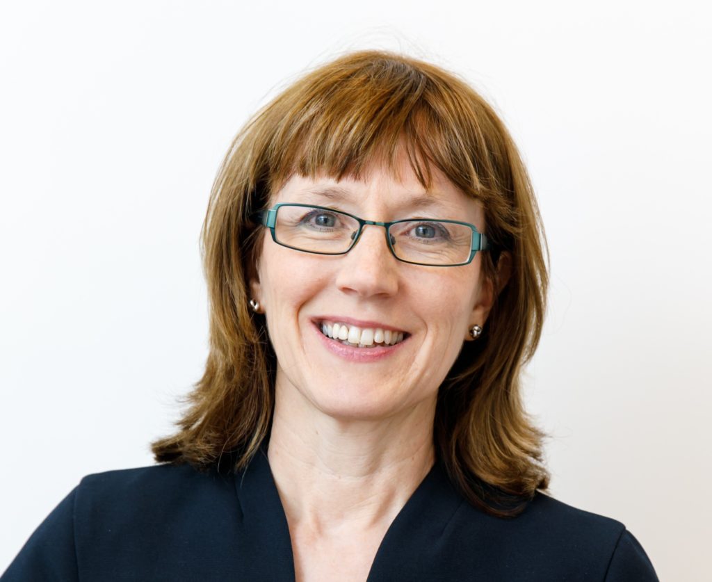 Image is a head and shoulders image of Philippa smiling at the camera. Philippa is wearing a black top and glasses.