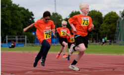 Photo of 4 young children in sportswear running outdoors on an athletic track.