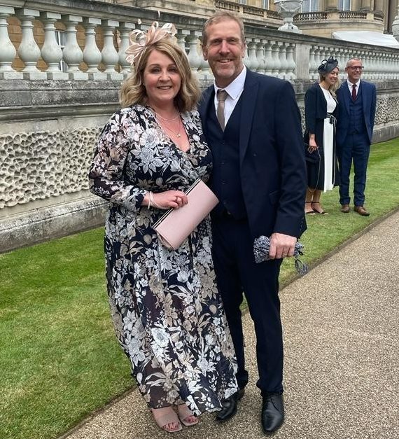 Alison Stannard in long black flowery dress and fascinator, holding a clutch bag at the Royal garden party.