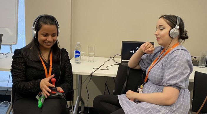 Nadia Patel (Learning and Skills Co-ordinator, Galloways Society for the Blind) and Fatima Rifai (Support Assistant, Galloway's Society for the Blind). Nadia plays the audio game with a joystick controller, while Fatima listens in, via headphones. Copyright: Lancaster University.