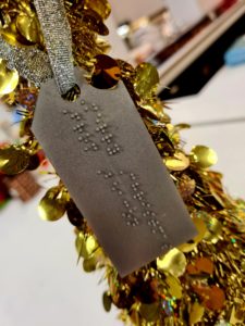 A gold, braille gift tag attached to a gold Christmas tree