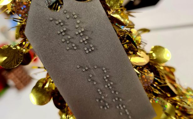 A gold, braille gift tag attached to a gold Christmas tress