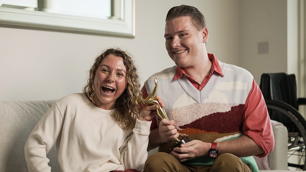 Ella (Emily Nicole Roberts) and Sam (Jake Sawyers) holding a trophy in comedy The i-Word.