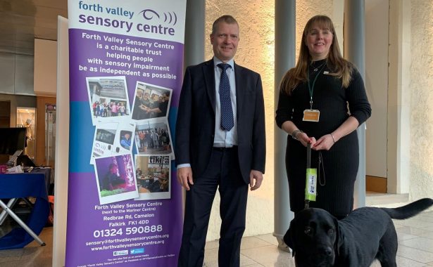 Laura Cluxton with guide dog Sadie and Graham Simpson MSP standing by Forth Valley Sensory Centre exhibition stand.
