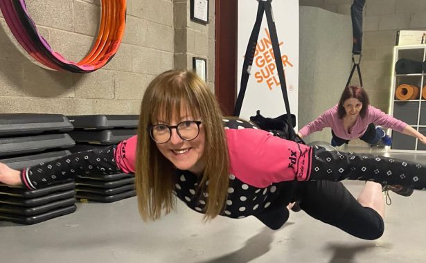 Two women wearing a harness in a Bungee Super Fly fitness class indoors hovering over the ground slightly.