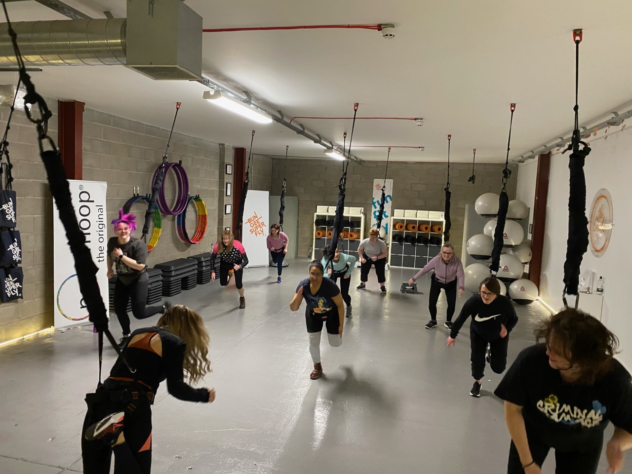 Indoor Bungee Super Fly fitness class with everyone running in harnesses and rope attached to ceiling. 