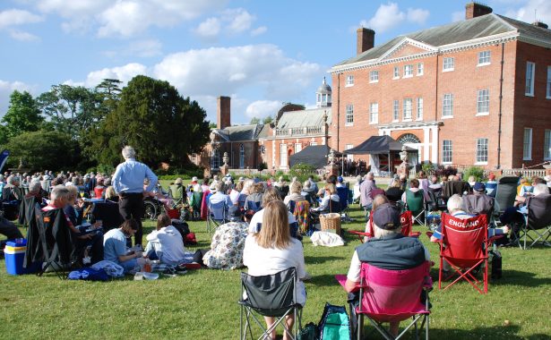 People sitting in the grounds of the National Trust’s Hatchlands Park House on a sunny day, enjoying Music in the Park.