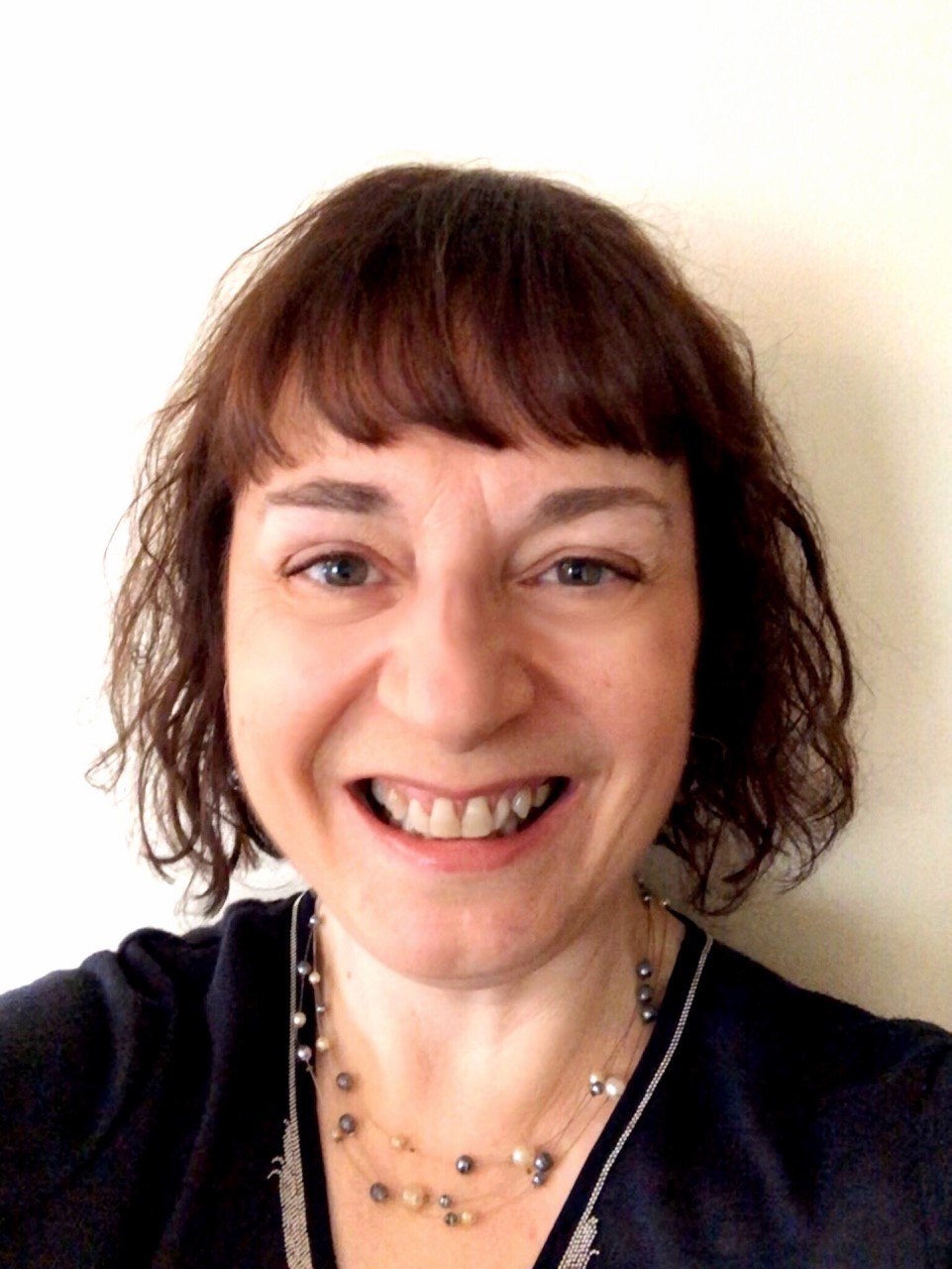 smiling, wearing a black top and a white and grey beaded necklace.