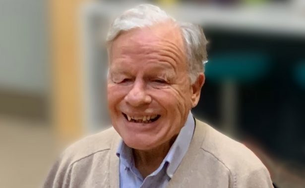 Mike Townsend with a big, warm smile, wearing a blue shirt and beige cardigan.