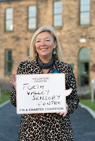 Jacquie holding a sign which says "Volunteers charter. Forth Valley Sensory Centre. I'm a charter champion."