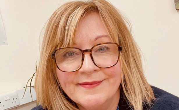 Alison Stannard smiling, wearing large framed tortoise shell glasses.