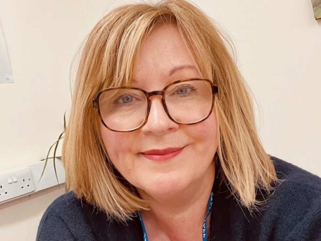 Alison Stannard smiling, wearing large framed tortoise shell glasses.