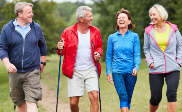 Two men and two women in leisure outfits, laughing and smiling whilst walking outdoors with trees in the background.