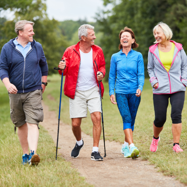 Two men and two women in leisure outfits, laughing and smiling whilst walking outdoors with trees in the background.