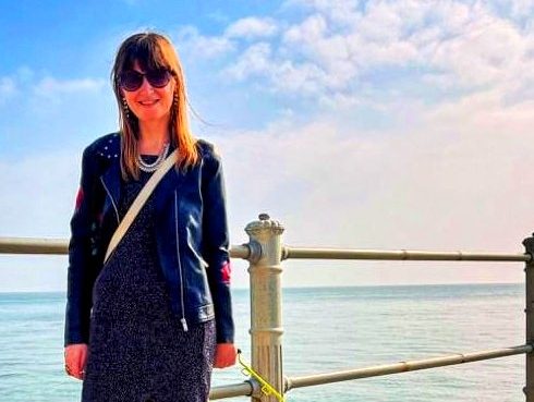 Fern is standing on a path next to the sea on a bright sunny day.