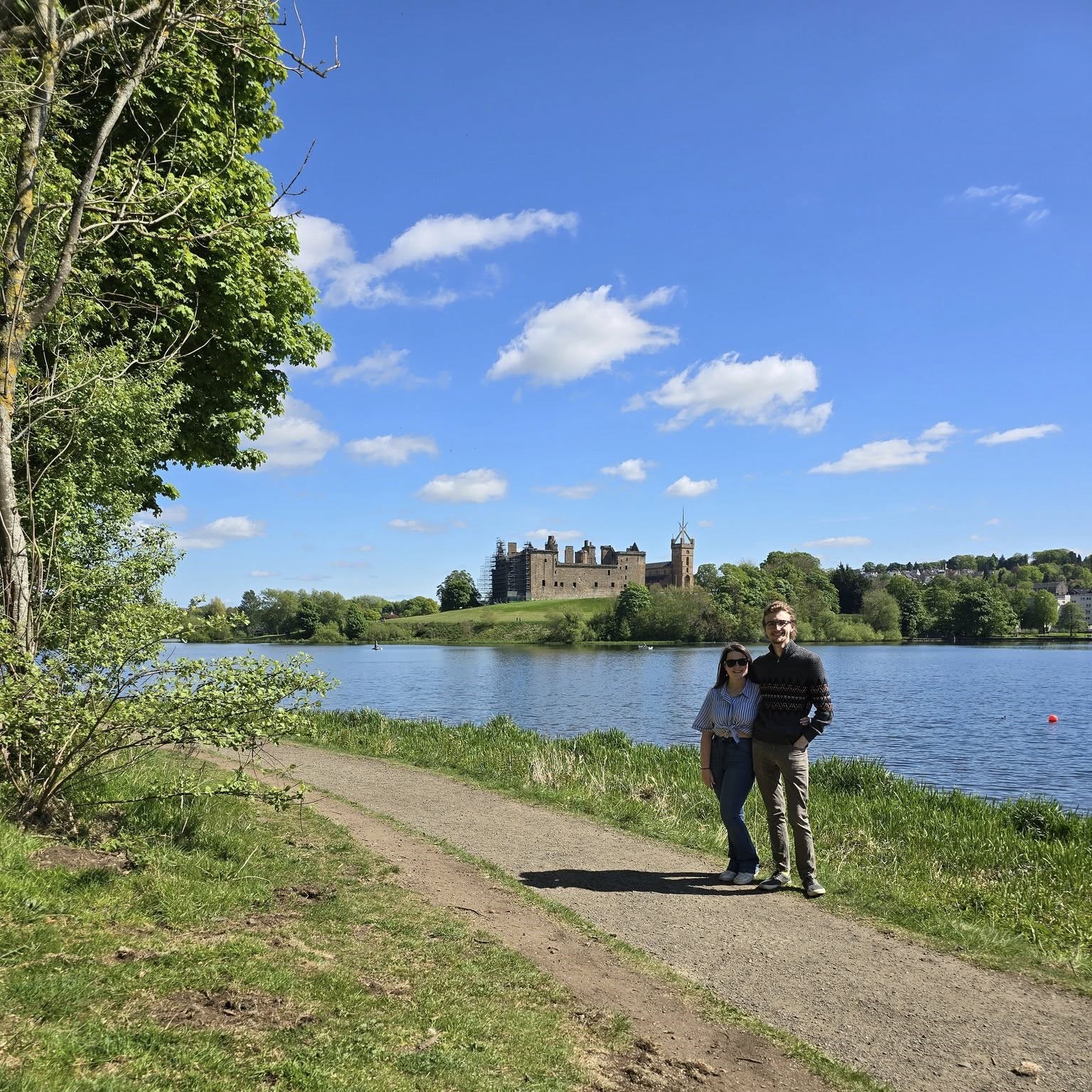 Melissa, FVSC Youth and Family Support Worker with her fiance Michael walking at Linlithgow Loch on a sunny day. Linlithgow Castle is in the distance across the loch.