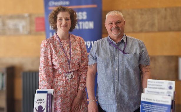Our Sight Loss Information Officers, Ash and Hayley smiling and standing in front of a table full of information leaflets.