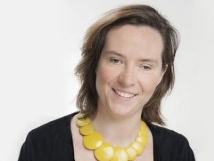 Eleanor is smiling and is wearing a black top with a yellow necklace with overlapping discs. Eleanor is smiling and is wearing a black top with a yellow necklace with overlapping discs.
