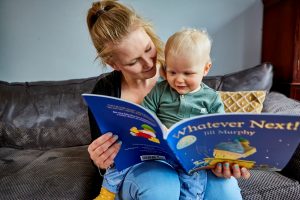 A mother sits with her young child reading a children’s book