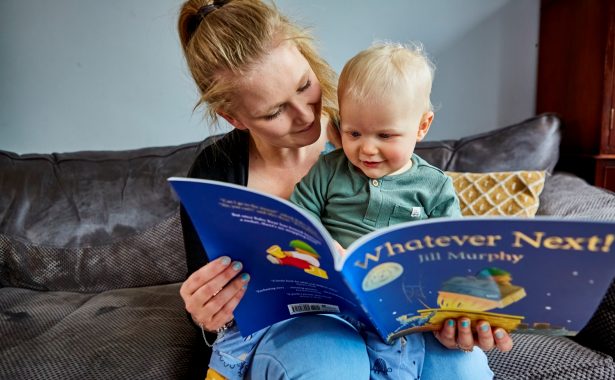A mother sits with her young child reading a children’s book