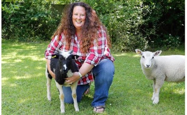 Beth is crouching and holding her young black and white sheep and her young white sheet is on the right.