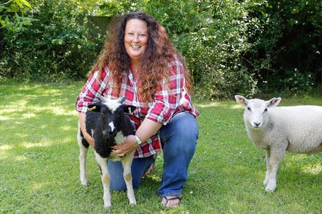 Beth is crouching and holding her young black and white sheep and her young white sheet is on the right.