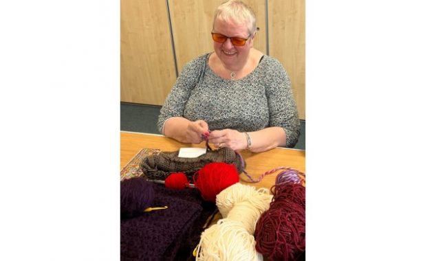Lawson Eades knitting at a table with red, burgundy and white balls of yarn.