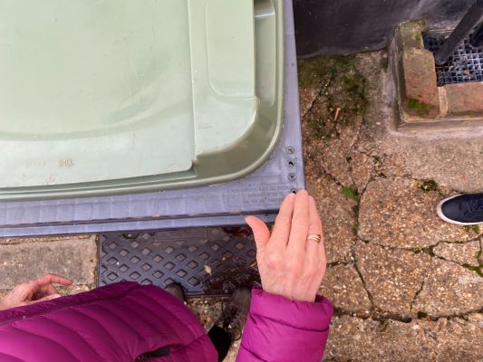 A hand touching the corner of a bin which has 4 holes drilled into it.
