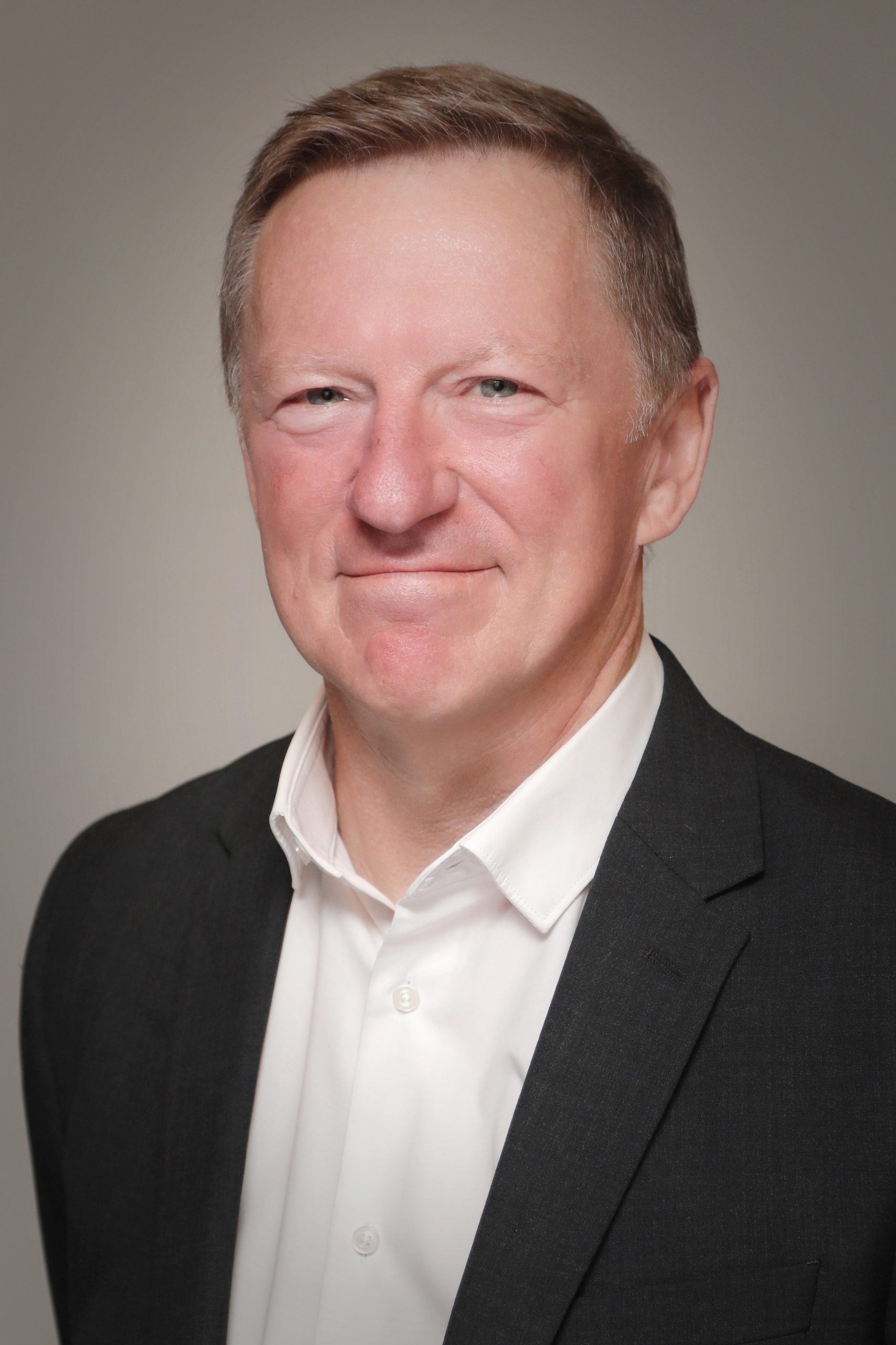 Simon is smiling and wearing a white shirt and black blazer.