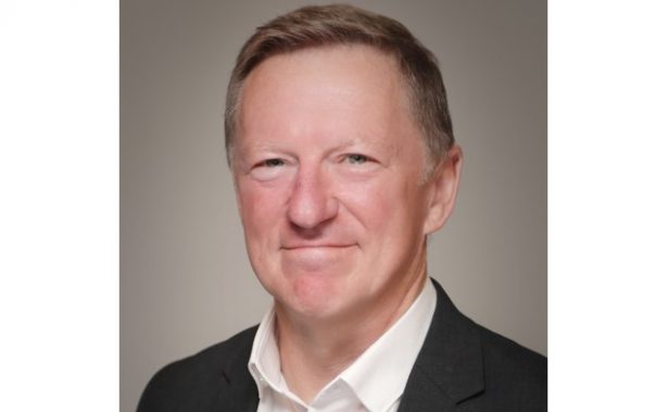 Simon is smiling and wearing a white shirt and black blazer.