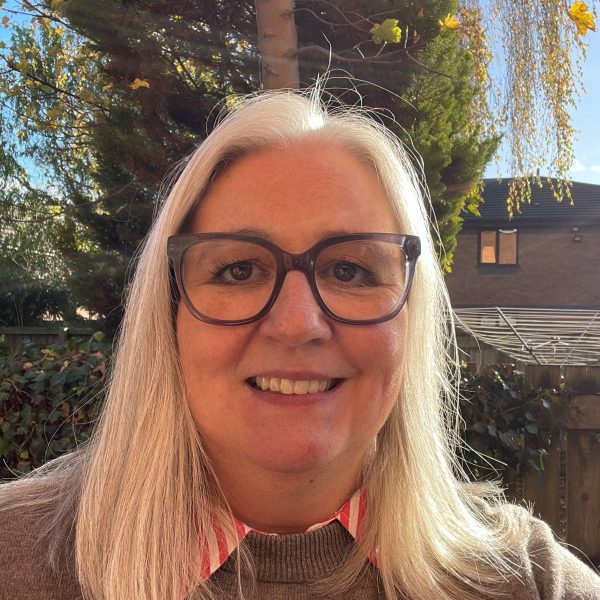 Lowri smiling, wearing glasses with black frame with her blond hair sitting on her shoulder