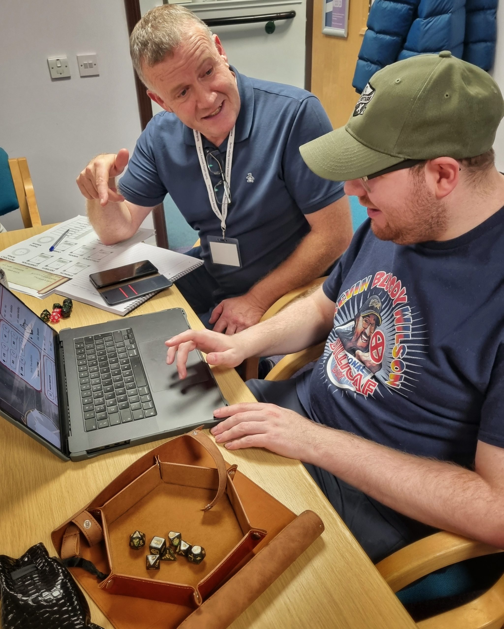 Kyle and John sitting in front of a laptop with Dungeons & Dragons dice to the left.