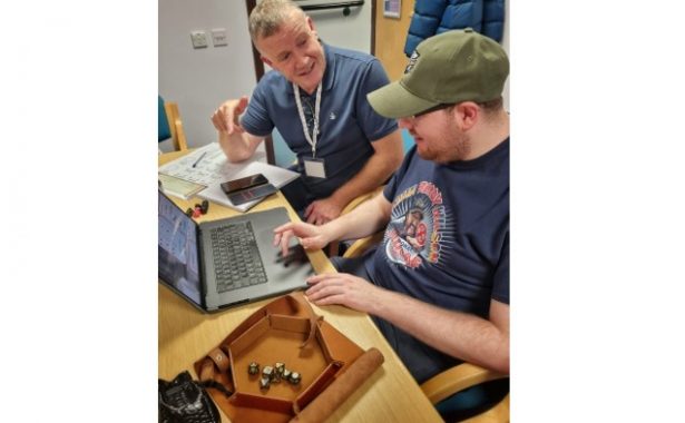 Kyle and John sitting in front of a laptop with Dungeons & Dragons dice to the left.