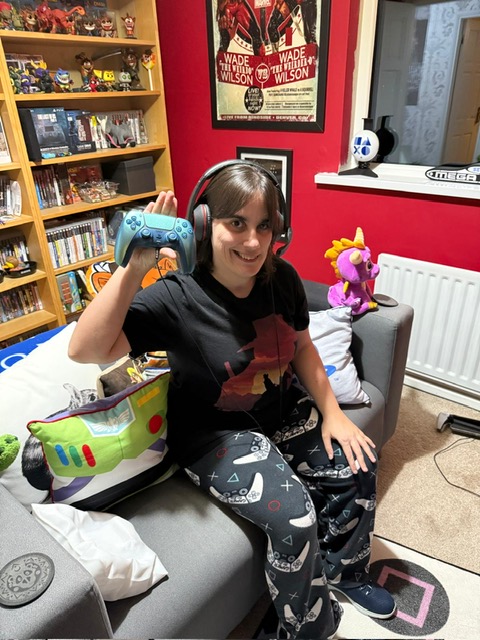 Louise Meeke sitting on her bed smiling and holding up her PS5 controller