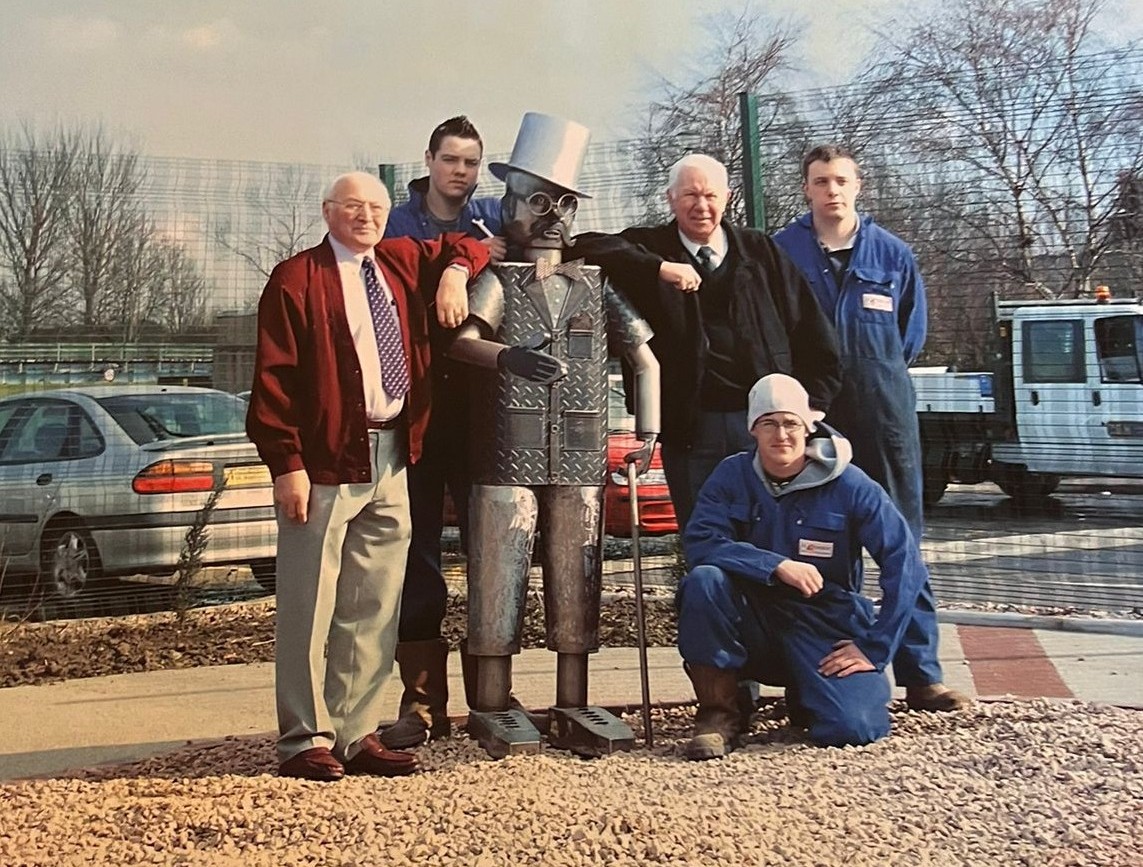 Douglas the Tin Man on installation in the sensory garden, with Tom Binnie (left) and Ian Cruickshanks leaning on his shoulders and two apprentices who helped build him standing behind the sculpture, with another apprentice kneeling in front.