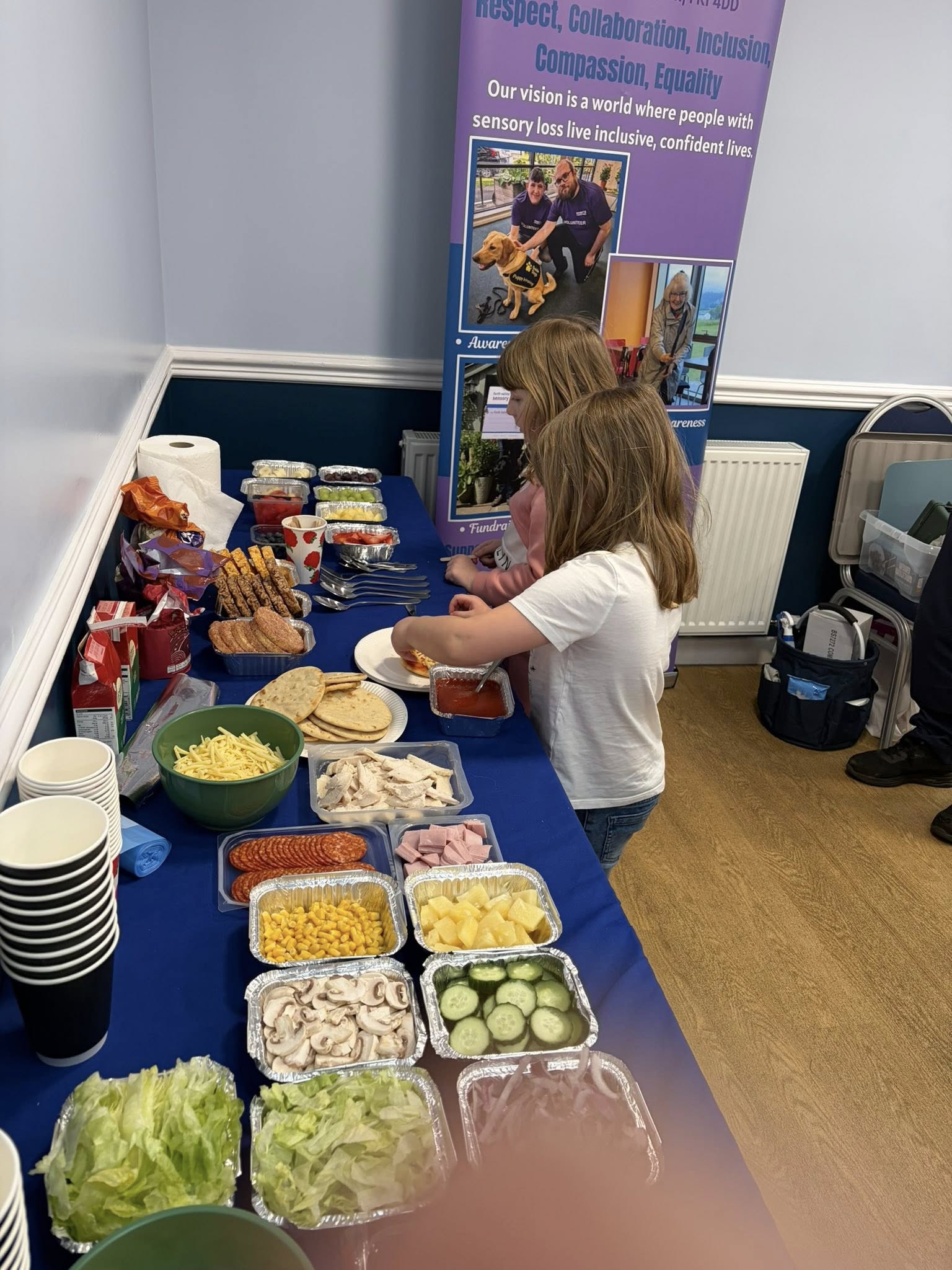 two young girls making their own pizzas from the ingredients laid out.