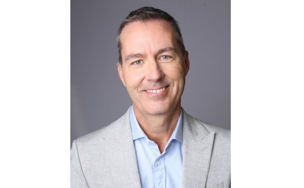 Richard smiles warmly with head slightly tilted to the side. He is wearing a light blue shirt and light grey blazer.