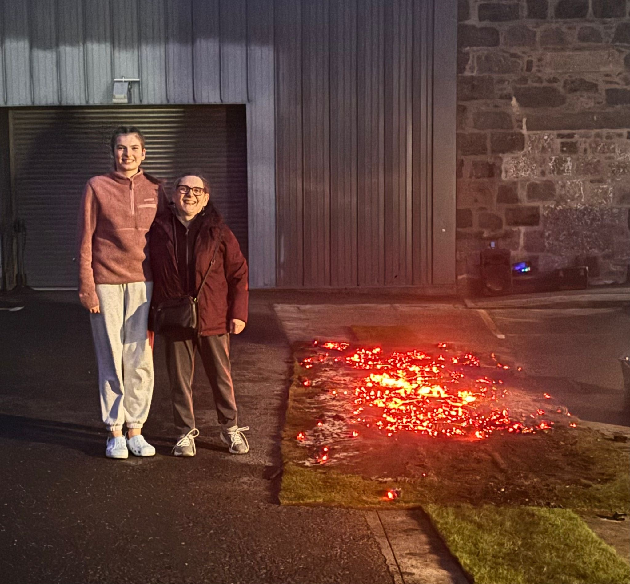 YPSS member Talijah Reinholde and NESS added value services manager Sheila Ogden standing together smiling, to the left of the firewalk coals.