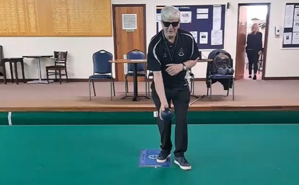 David Cox wearing Rayban Meta glasses and bowling kit standing on an indoor bowling green, holding a bowl in one had ready to bowl.