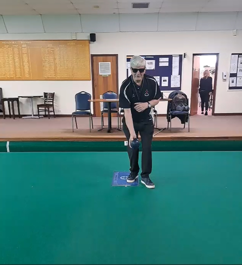 David Cox wearing Rayban Meta glasses and bowling kit standing on an indoor bowling green, holding a bowl in one had ready to bowl.