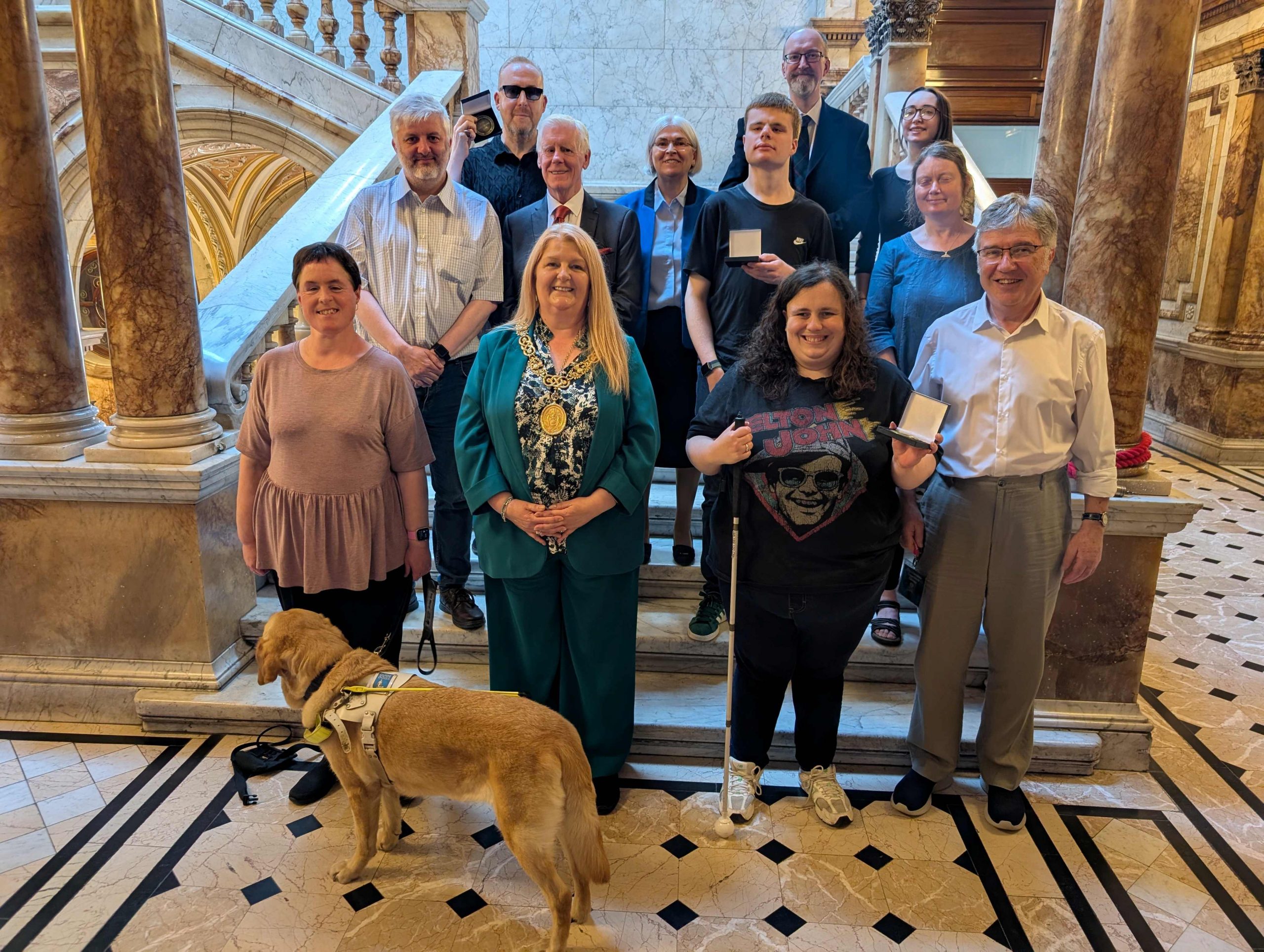 Group photo, participants holding medals. Bottom row left to right: Jen Worral (participant, with guide dog Snowball), Lord Provost, Claire Forde (participant), John McArthur (Glasgow Speakers Club), middle row: James Adams (Director, RNIB Scotland), Cllr Robert Mooney (sponsor), Luke Teasdale (participant), Morag Wilson (participant), Back row: Robert King (participant), Grace Hendry-Nash (Glasgow Speakers Club), Bobby Livingston (GSC), and Iona Adamson (RNIB Scotland volunteer).