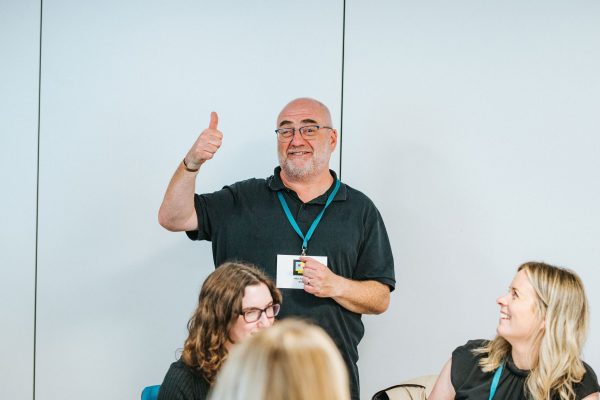 A male workshop facilitators standing giving a thumbs up