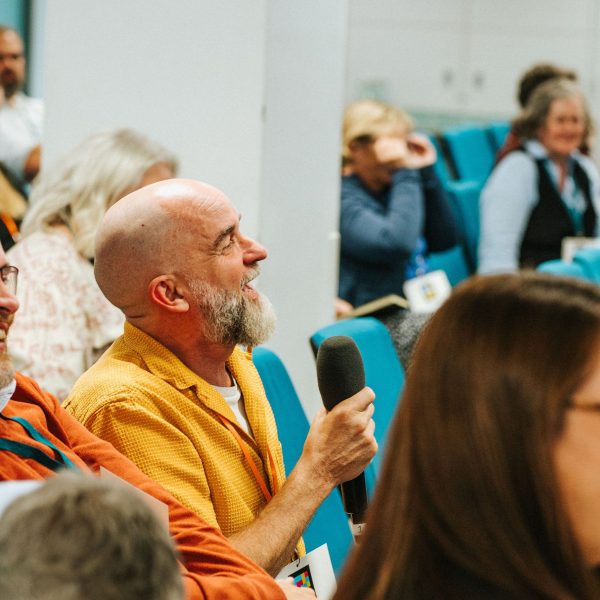 Audience from 2025 annual conference keynote session. A delegate is holding a microphone and asking a question