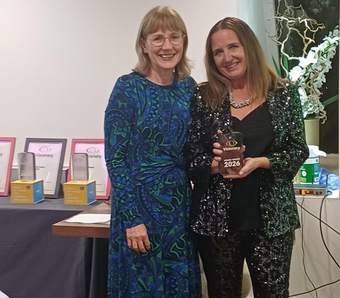 Philippa Simkiss from Specsavers is smiling, next to Kirstie Thomas from 4Sight Vision Support who is holding a trophy.