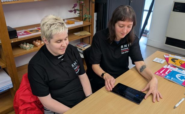 Glasgow Tech Hub volunteers Rosie and Emily sitting at a desk, looking at an electronic device.