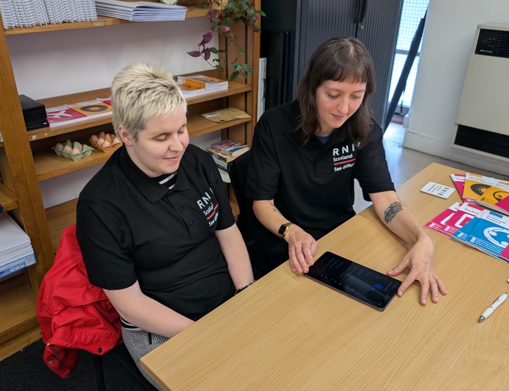 Glasgow Tech Hub volunteers Rosie and Emily sitting at a desk, looking at an electronic device.