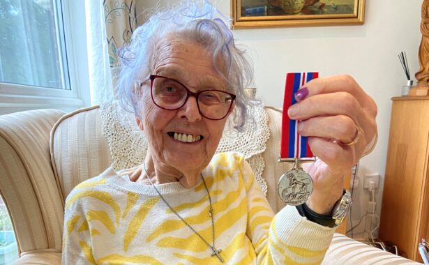 Gwenneth Pedler is sitting on a sofa, holding a medal.